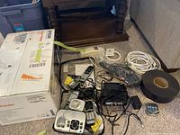 Photo showing the Epson printer box alongside various electronics including phones, remote controls, and cables.