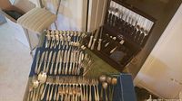 Wide view of complete collection of various silver plate cutlery laid out on a white surface, also includes large serving utensils and carving set.