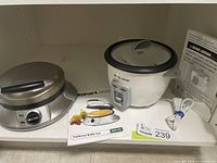 Photo showing the waffle iron, rice cooker, their power cords, and user manuals placed side by side on a shelf.