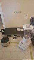 Lot of three small kitchen appliances including a white Hamilton Beach blender, an Oster electric griddle with dual handles, and a small white Crock-Pot slow cooker.