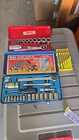 Two ratchet socket sets in red and blue steel cases with sockets, ratchets, extension bars, and a small yellow case with bits.
