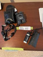Photo showing both the Bushnell binoculars with strap and case and the Bushnell spotting scope with pouch on a wooden surface.