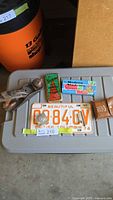Overview of lot showing vintage British Columbia license plate, protractor sets, tape measure, block plane, and pins