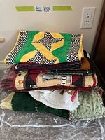 Stack of colorful handmade quilts and quilted items folded on a table, showing a range of patchwork patterns and vibrant fabric colors.