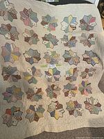 Full view of the vintage quilt showing multiple flower-shaped patchwork blocks in assorted pastel and muted fabrics on a cream background.