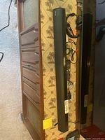 Photo showing the full length of the VMAI sound bar laid next to a TV stand. Black remote control and headphones visible beside it.