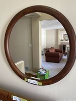 Front view of round wood framed mirror hanging on a wall, showing reflection of a living room.