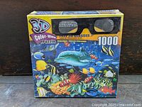 Front view of the 3D Color-View puzzle box showing underwater scene with dolphin and fish, box states 1000 pieces and includes 3D glasses.