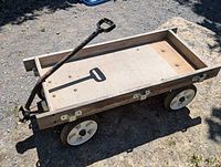 Clear side angle photo showing full vintage wooden wagon with metal handle and wheels outdoors on dirt surface.