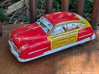 Front-side angle view of red tin litho car showing woodgrain panels and driver illustration