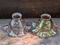 Front view of two iridescent carnival glass lampshades with floral pattern and ruffled edges.