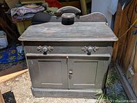 Front angled view of early pine washstand showing top surface, drawer with knobs, and two lower cabinet doors.