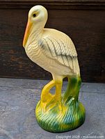 Chalkware pelican figurine on a tabletop surface with wooden background, showing front and side view.