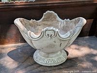 Front and angled views of the cement planter showing its ornate design and weathered finish.