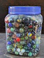 Front view of jar packed with assorted colored glass marbles with blue lid.