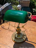 Old brass base desk lamp with green glass rectangular shade and pull chain on table in outdoor setting.
