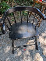 Front angled view of the black wooden child's captain's chair showing its curved spindle back, contoured seat, painted black finish with wear marks, and the turned legs with horizontal support.