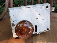 Close-up photo showing metal lock body painted white with paint chipping and a single brown mottled ceramic door knob.