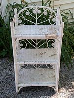 Front view of the old white wicker bookcase showing wear, discoloration, and chipped paint on shelves and sides.