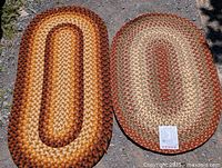 Photo showing two oval braided rugs side by side outdoors on gravel, the new one on the left in warm tones and the older one on the right in muted earth tones.