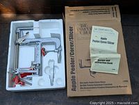 Apple peeler, corer, and slicer device in a white plastic tray, with original packaging and instruction booklet on the side.