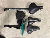 Overhead view of four saddles, two seatposts and saddle cover on concrete floor