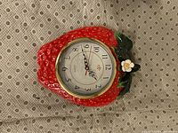 Front view of strawberry-shaped wall clock showing dial, hands, and decorative fruit design
