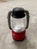 Front view of red battery-operated lantern showing clear globe, black cap, grey handles