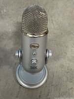 Front view of Blue Yeti microphone showing logo, mute button, gain knob, THX logo, stand