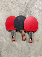 Three ping pong paddles on concrete floor showing faces and handles