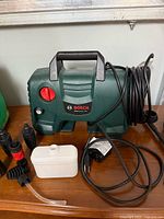 Bosch pressure washer unit with power cord, detergent bottle, hose and nozzles visible