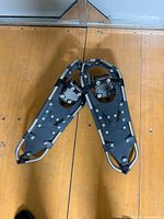 Pair of grey aluminum snowshoes side by side on floor