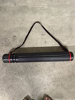 Full view of telescopic black plastic tube with red rings and shoulder strap