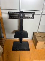 Overall view of black freestanding TV mount stand showing bracket, shelves and base