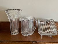 Photo of three crystal items: fluted vase, pitcher, and square bowl arranged on wooden surface