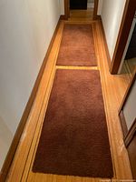 Photo showing two brown carpet runners with plush texture laid out in a narrow hallway.