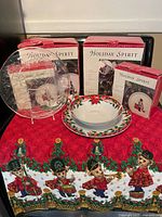 Overall view of Holiday Spirit themed Christmas tableware and textile including boxed sets and displayed plates, bowl, and tablecloth with teddy bear Christmas marching band design.