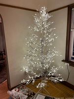Photo of white wire frame pre-lit Christmas tree standing on wooden floor with white lights illuminated
