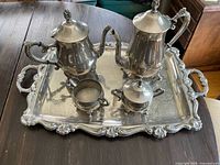 Photo of full silver plated coffee and tea service set on wooden table, including tray, coffee pot, teapot, creamer, and sugar bowl