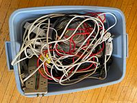 Photo of a large blue plastic container filled with a variety of electrical cords, extension cords, power bars, multi-plug adapters, video and computer cables tangled together.
