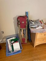 Photo showing red wrapping paper storage bag with rolls of wrapping paper inside next to plastic bins containing assorted greeting cards and gift bags.