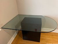 Glass top table with clear oval glass surface and black rectangular pedestal base shown from an angle