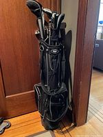 Full view of Voit golf bag showing multiple compartments, black with white trim, standing on hardwood floor.