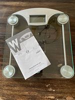 Weight Watchers digital glass scale on wooden surface with instruction manual placed on top.