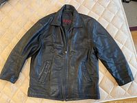 Front view of men's black leather jacket size XL, laid flat on beige surface.