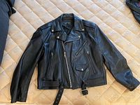 Black leather jacket laid flat showing front with zipper, pockets, collar, and waist belt.