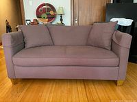 Medium brown loveseat with two cushions and wooden legs, shown in sofa form.