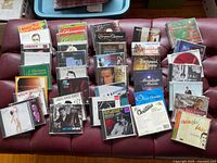 Photo showing multiple music CDs and vinyl records arranged on a couch with visible album titles and covers.