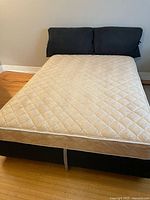 Full view of queen bed with mattress and two dark grey headboard cushions against wall