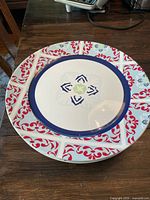 Two charger plates stacked: top plate white with blue and red pattern, bottom plate plain white.